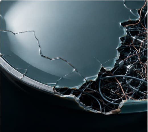A polished glass surface cracking at the edges, revealing a tangle of wires and structure underneath.